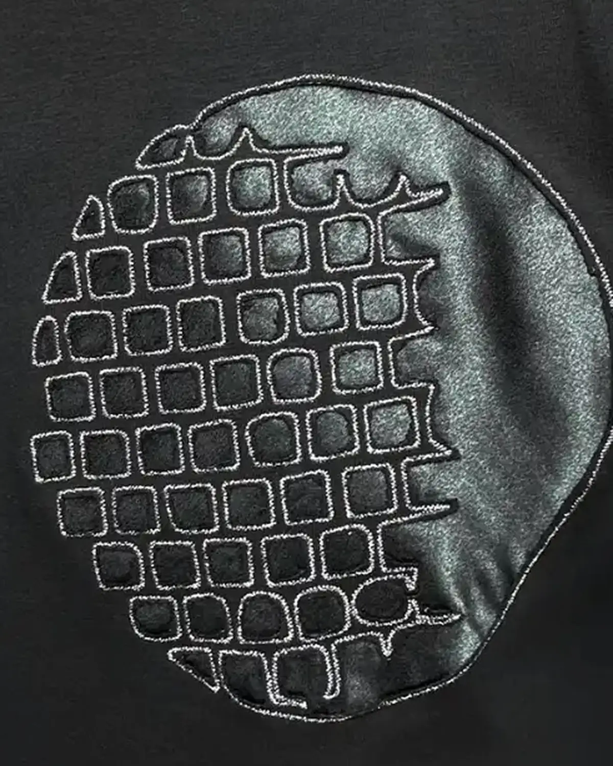 Black satin Monolit Geometry pillow cover, the geometric motif machine-embroidered into the fabric and held by tensioned thread.