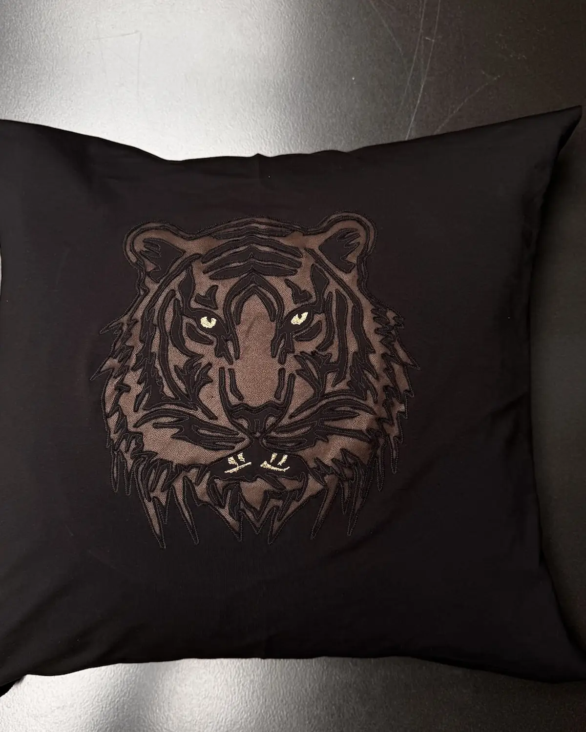 Black suede Monolit Tiger pillow cover, the tiger motif machine-embroidered with copper thread eyes and whiskers.