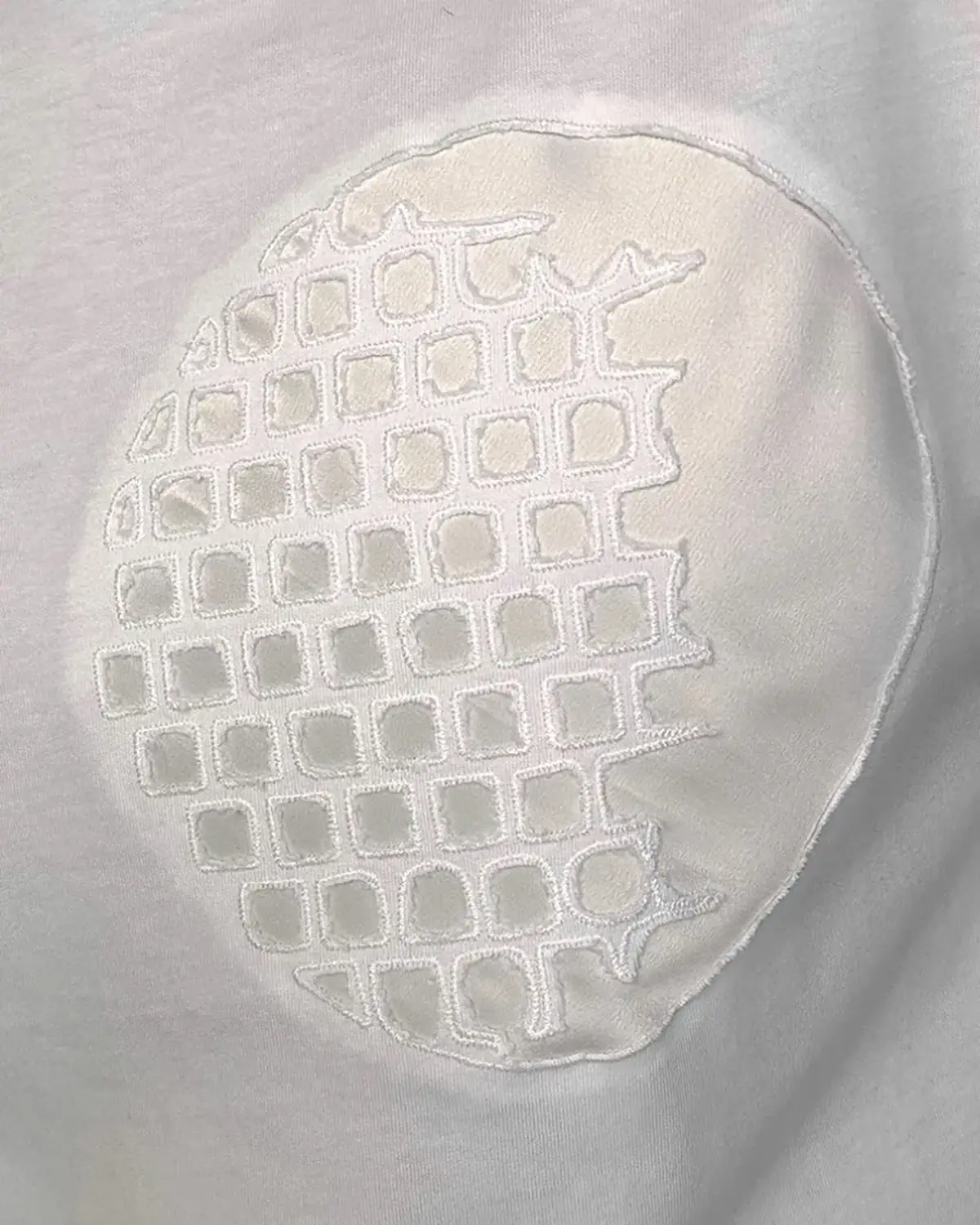 White satin Monolit Geometry pillow cover, the geometric motif machine-embroidered into the fabric and held by tensioned thread.